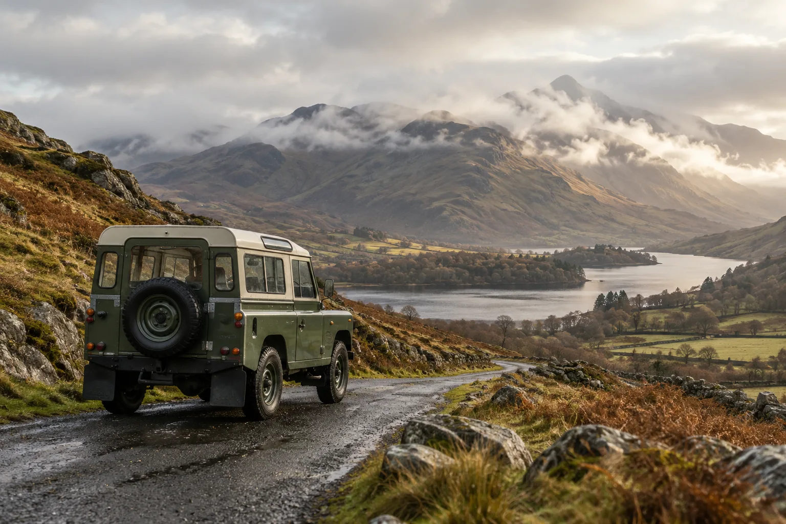 Classic olive off-road vehicle on a quiet Lake District road beside misty fells
